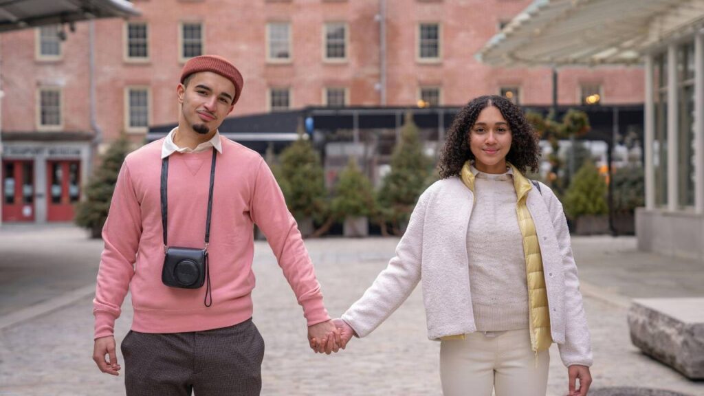 A young tourist couple smiling and holding hands while taking a photo together.